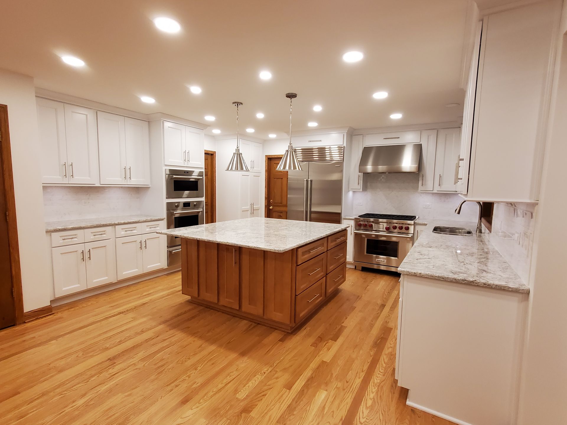 A kitchen with wooden floors , white cabinets , stainless steel appliances and a large island.