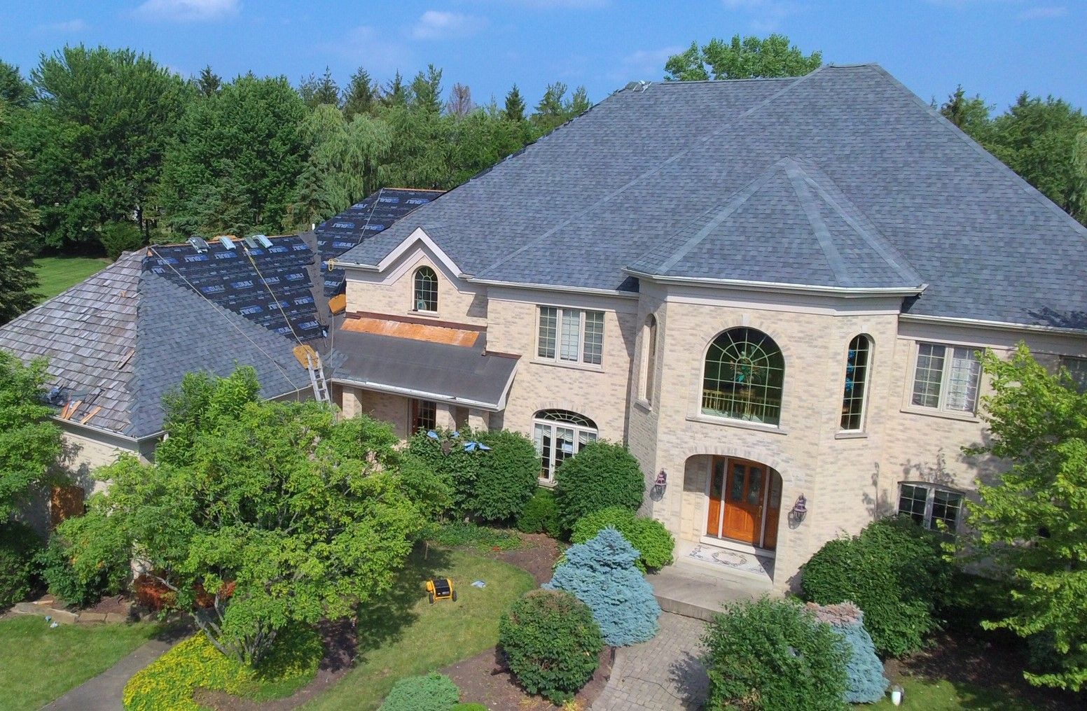 An aerial view of a large brick house with a gray roof surrounded by trees.