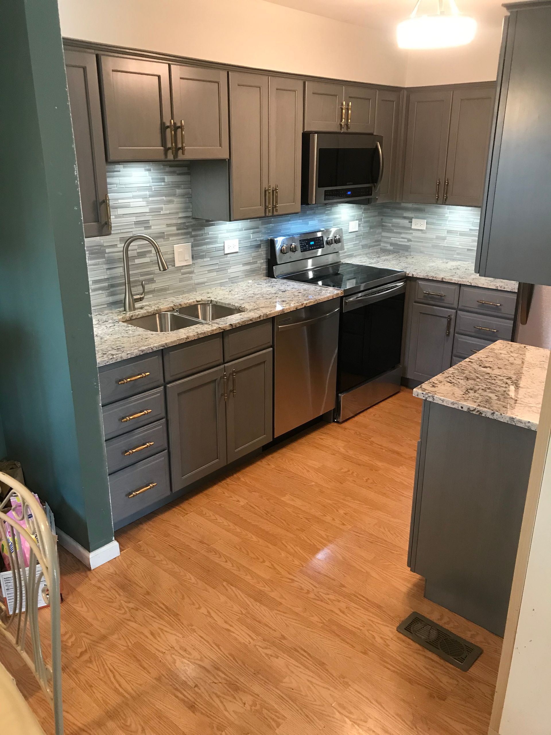 A kitchen with gray cabinets , granite counter tops , stainless steel appliances and a sink.
