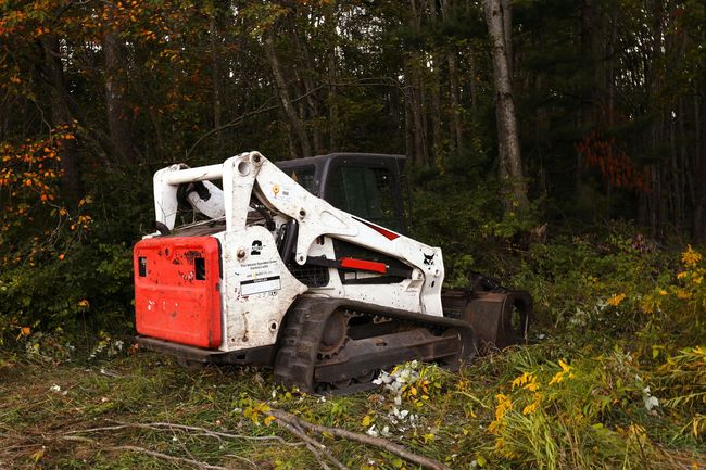 White and red skid-steer loader parked on a muddy forest edge