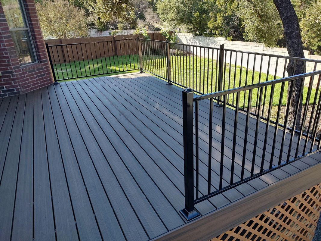 A composite deck with a wrought iron railing and a brick building in the background.