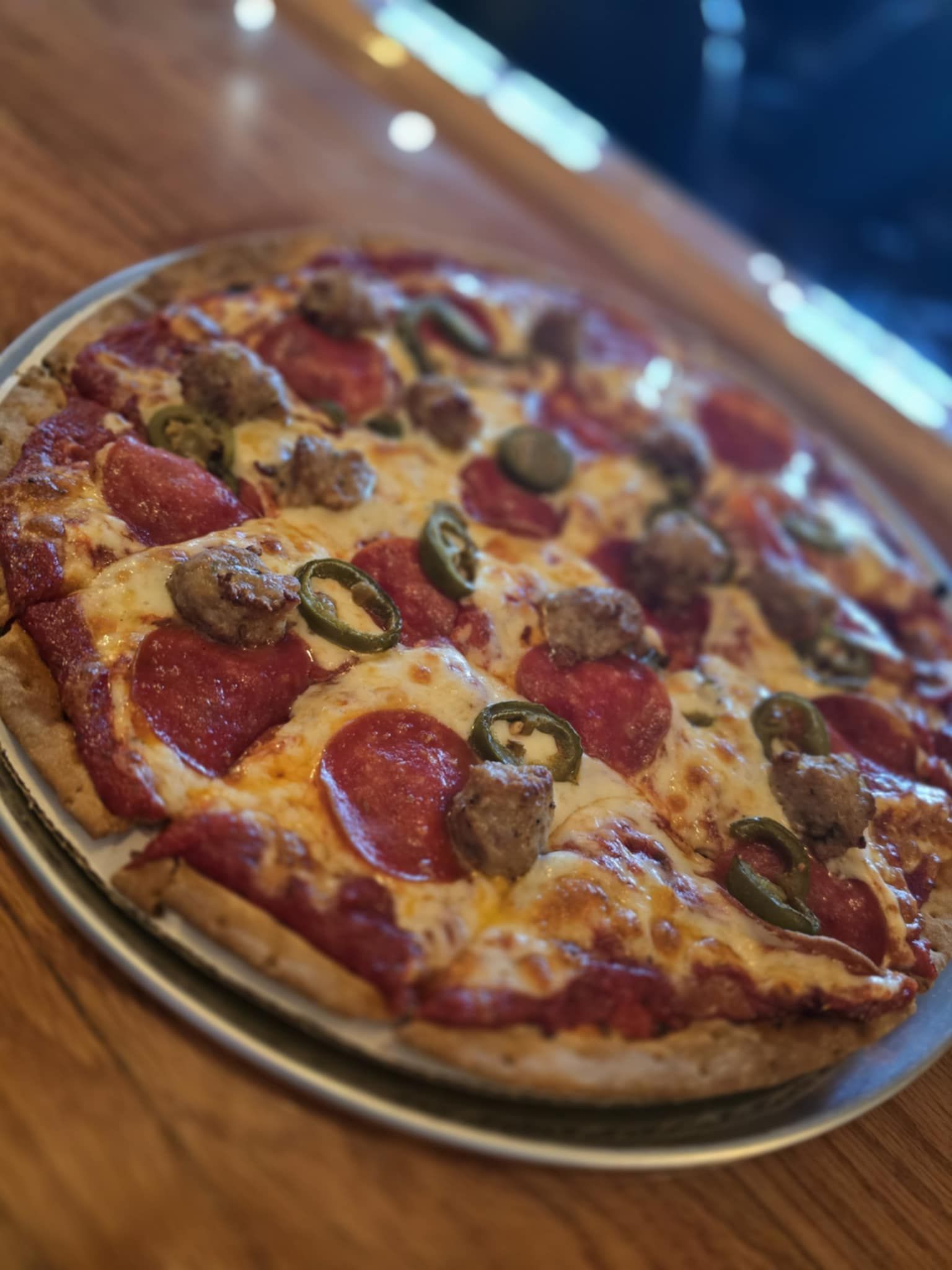 A pizza with pepperoni , sausage , jalapenos and cheese on a pan on a table.