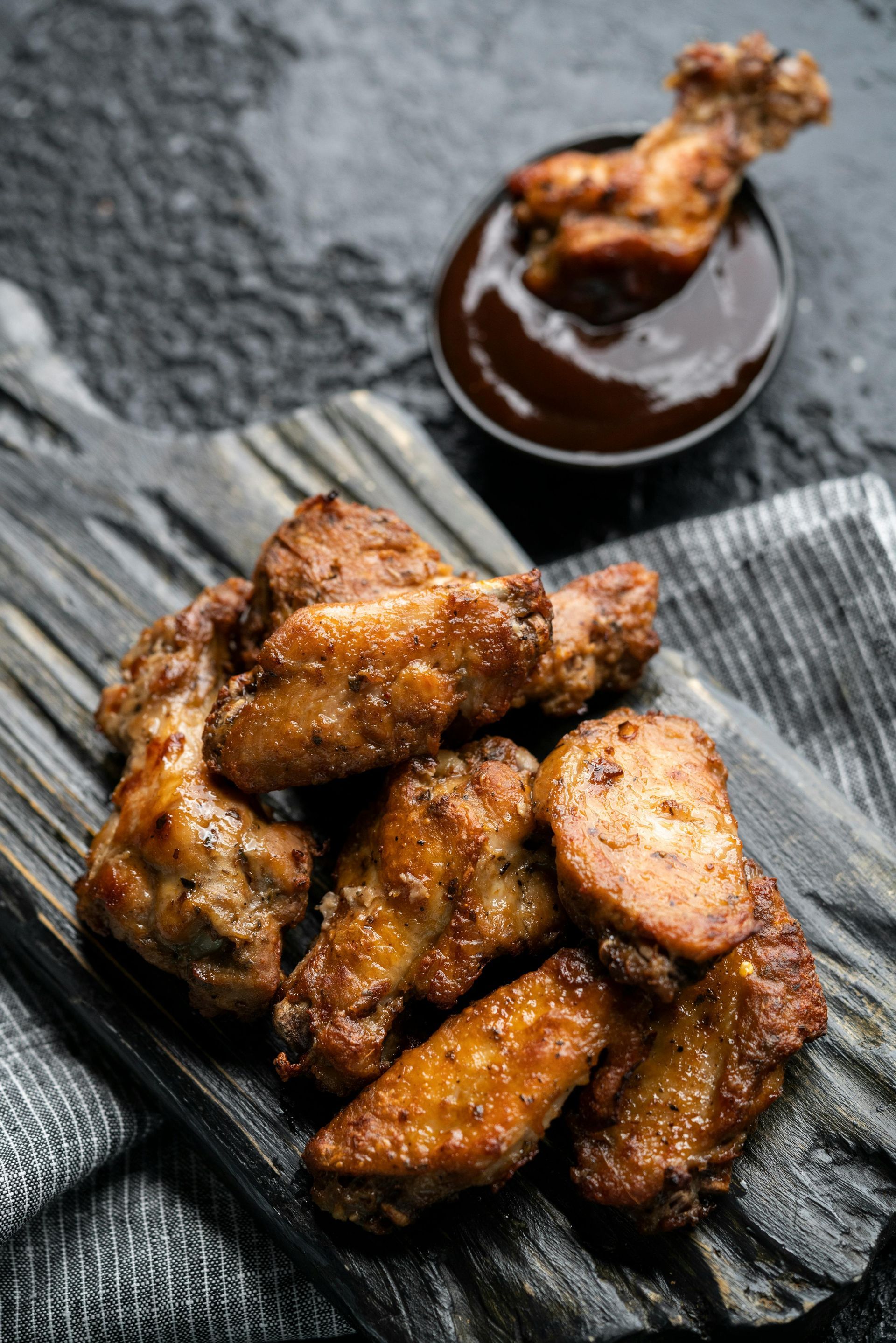 Fried chicken wings on a wooden cutting board next to a bowl of barbecue sauce.