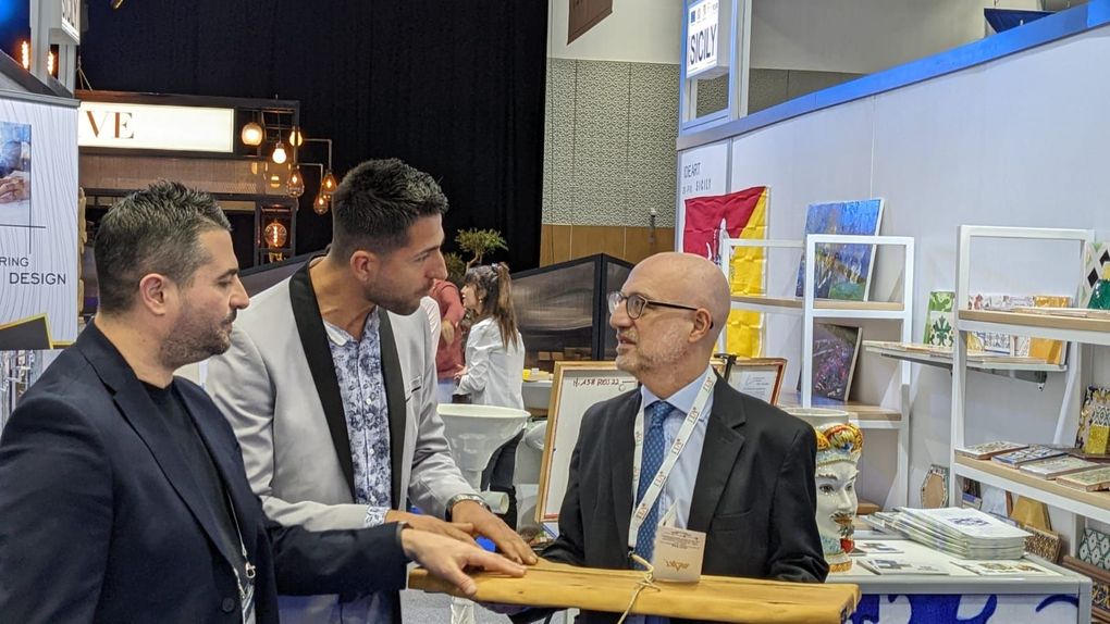 Tre uomini presso uno stand fieristico, che discutono di un'esposizione di prodotti.