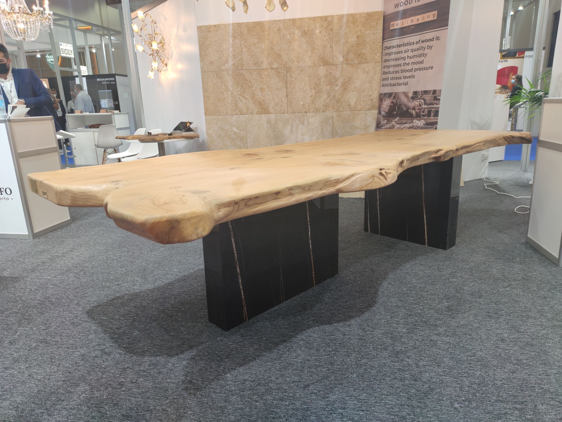 Grande tavolo in legno con bordo naturale su basi rettangolari nere in uno showroom.