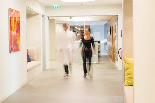 Ein Mann und eine Frau gehen einen Flur in einem Krankenhaus entlang.