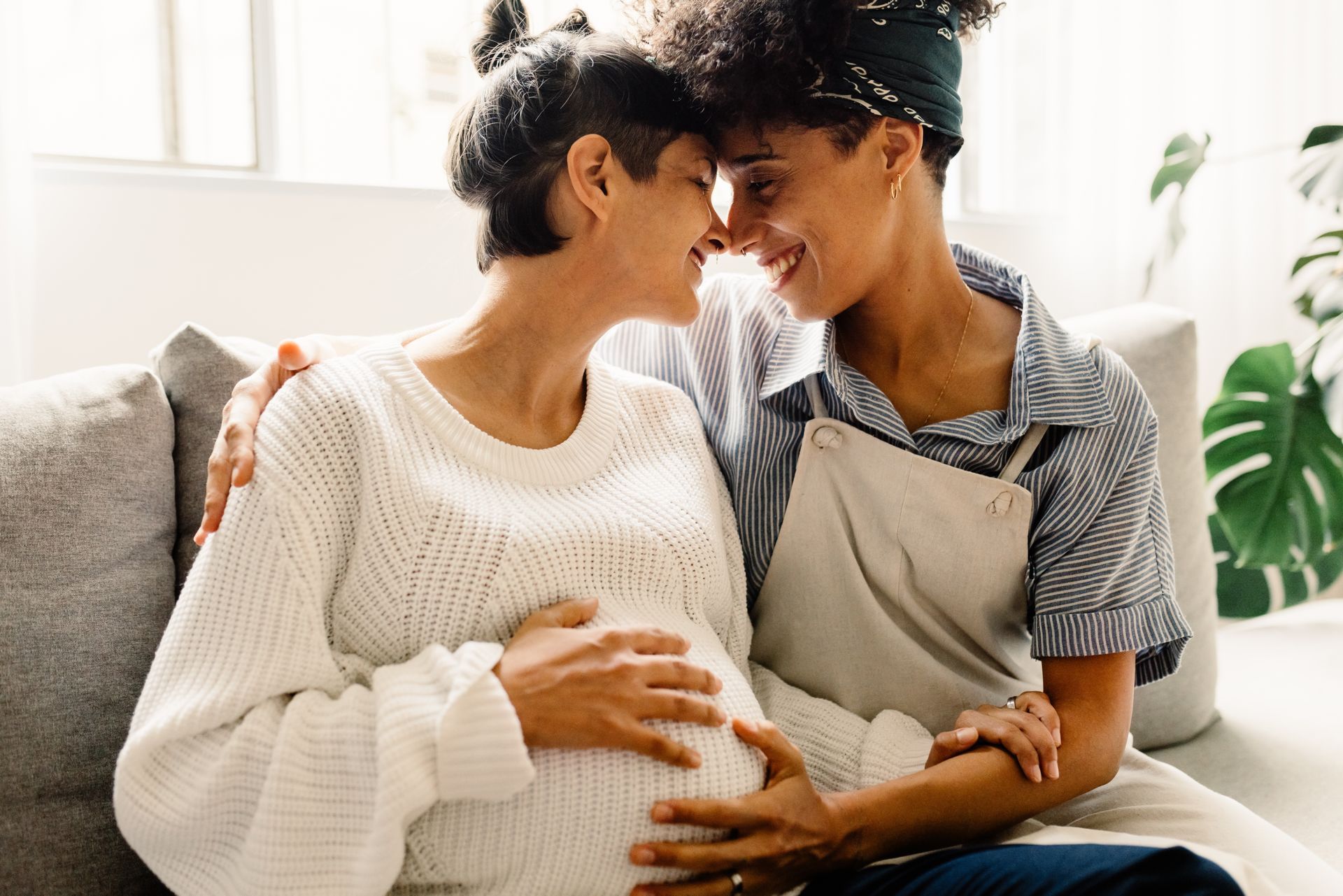 A pregnant woman is sitting on a couch with her partner another woman.