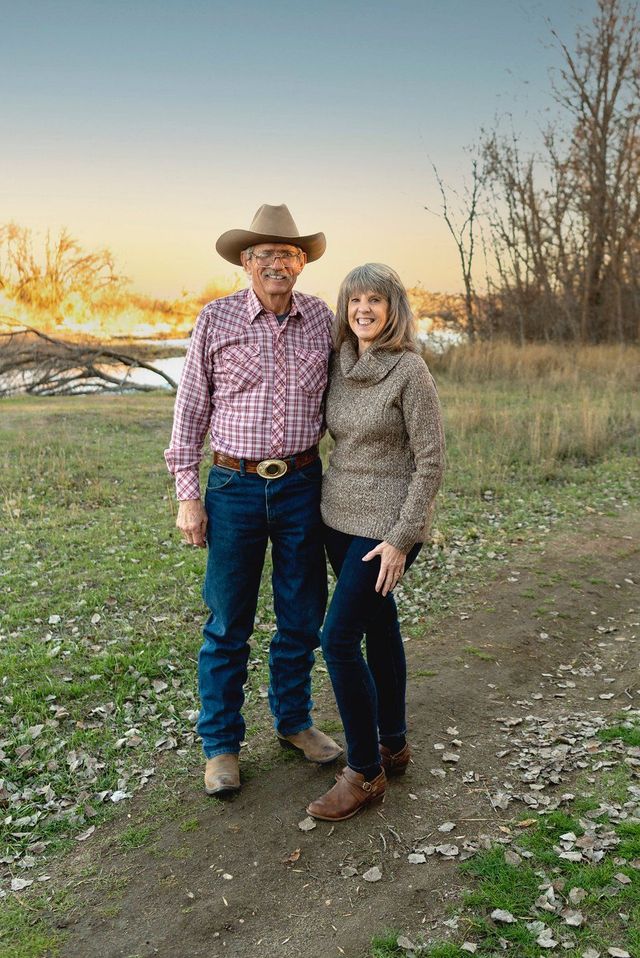 A man and a woman are standing next to each other in a field . the man is wearing a cowboy hat.