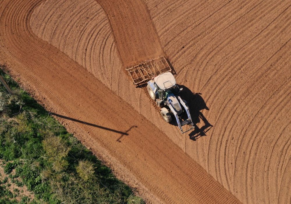 Tractor plowing a field, creating curved rows in brown earth. Aerial view.