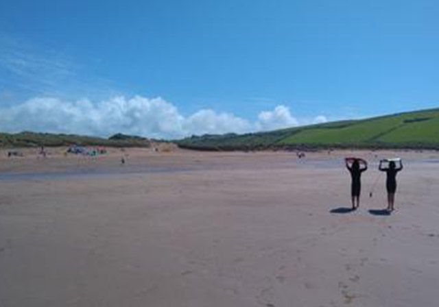 Two people holding surfboards on a sandy beach on a sunny day.
