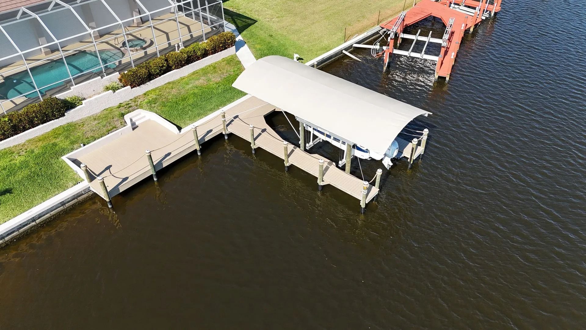Aerial view of a white-roofed dock pavilion extending into dark water beside a shoreline walkway