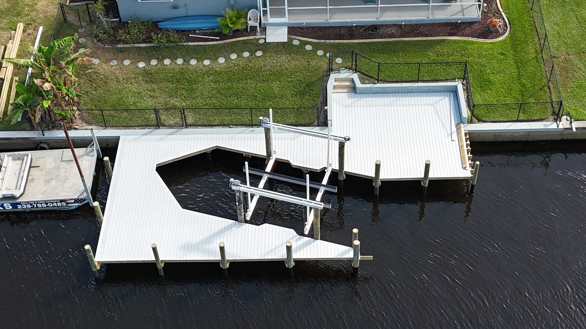 Aerial view of a white waterfront dock with stairs and railings beside dark water and grassy land.