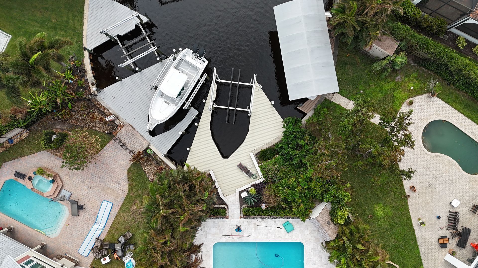 Aerial view of a waterfront patio with boats, dock, and several pools surrounded by tropical greenery.