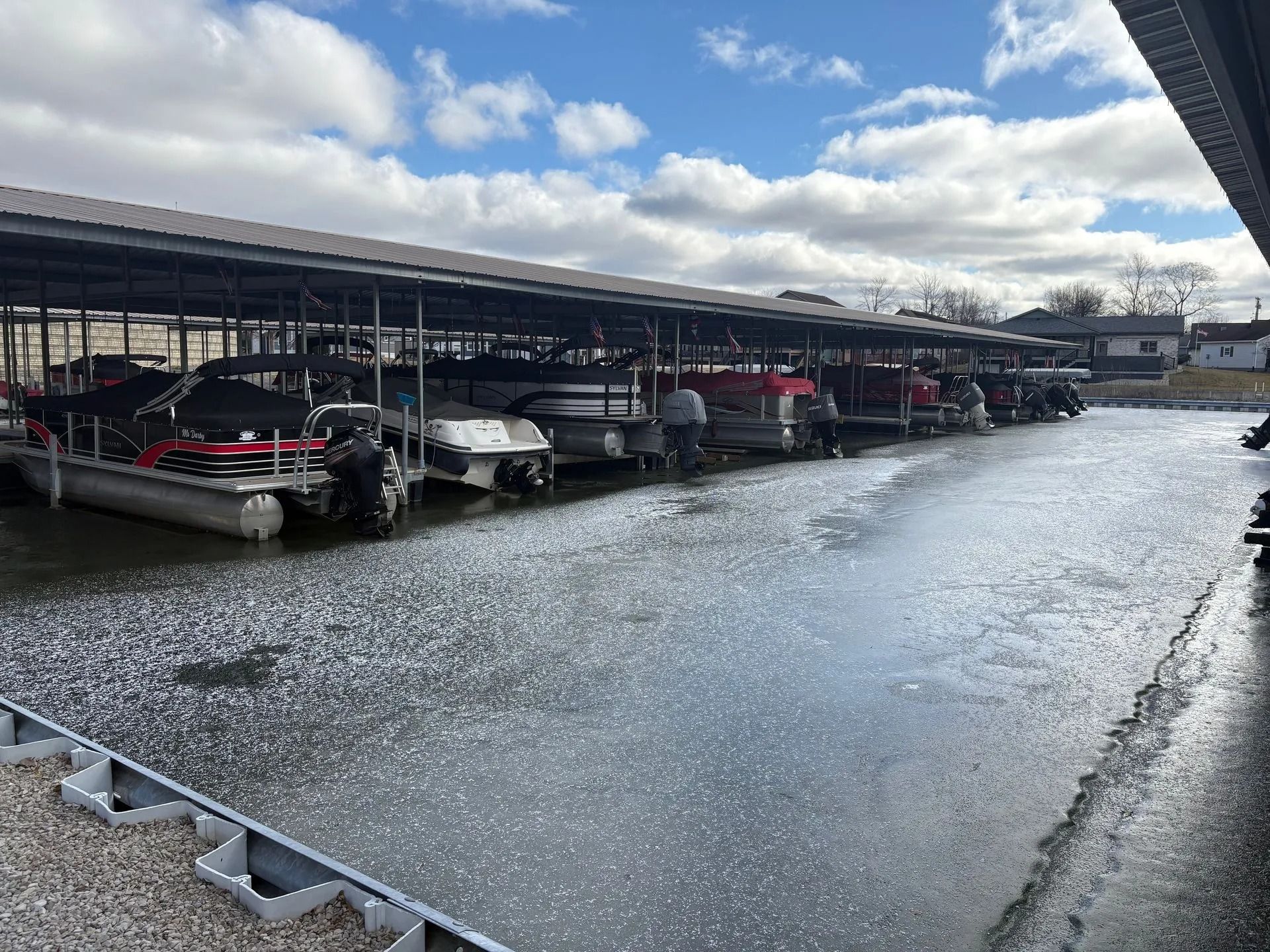 Covered marina with boats docked in wet slips under a cloudy sky.