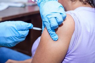Gloved healthcare worker giving a shoulder injection to a person in a sleeveless shirt