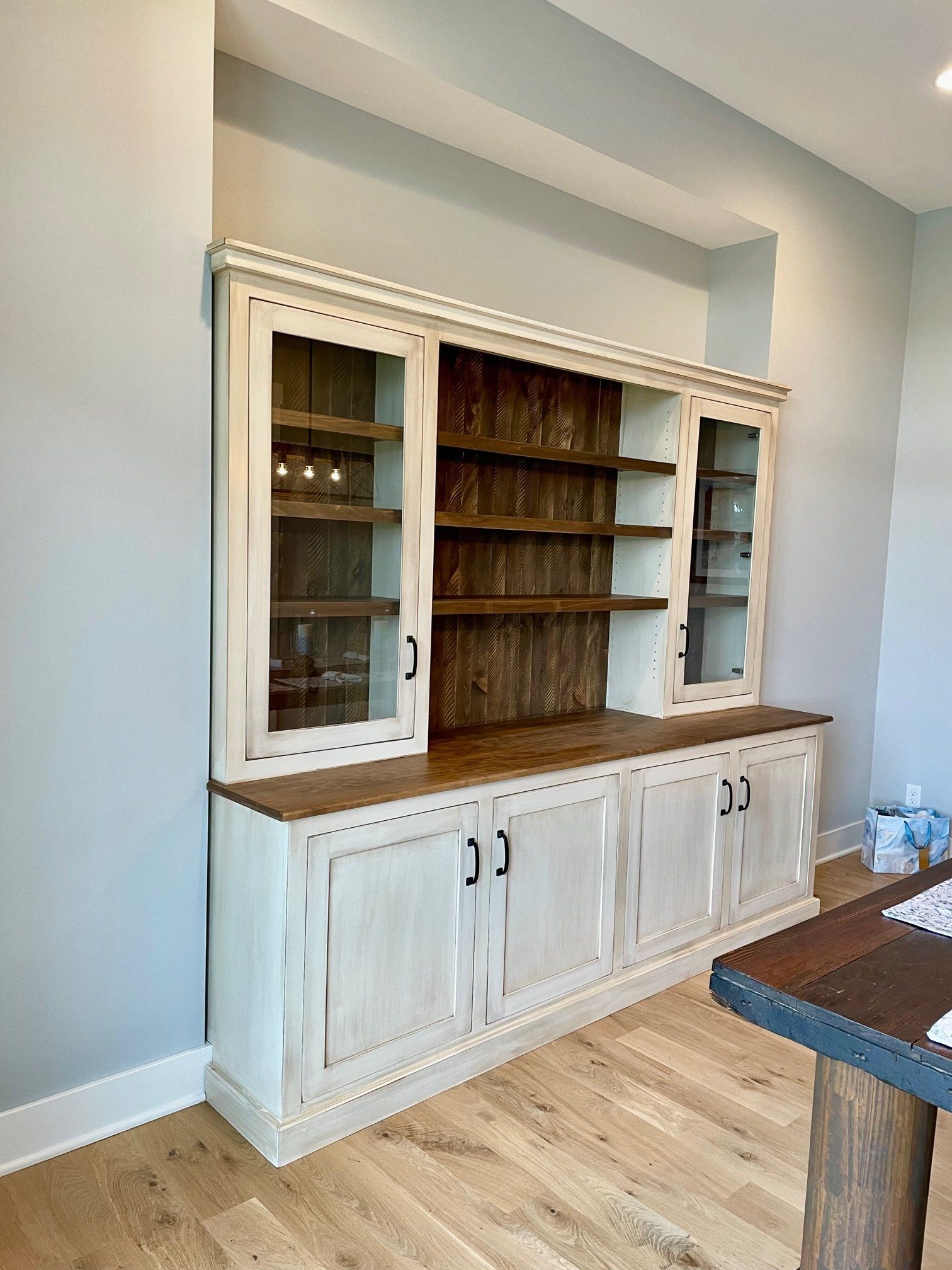 A large white cabinet with glass doors is in a room next to a wooden table.