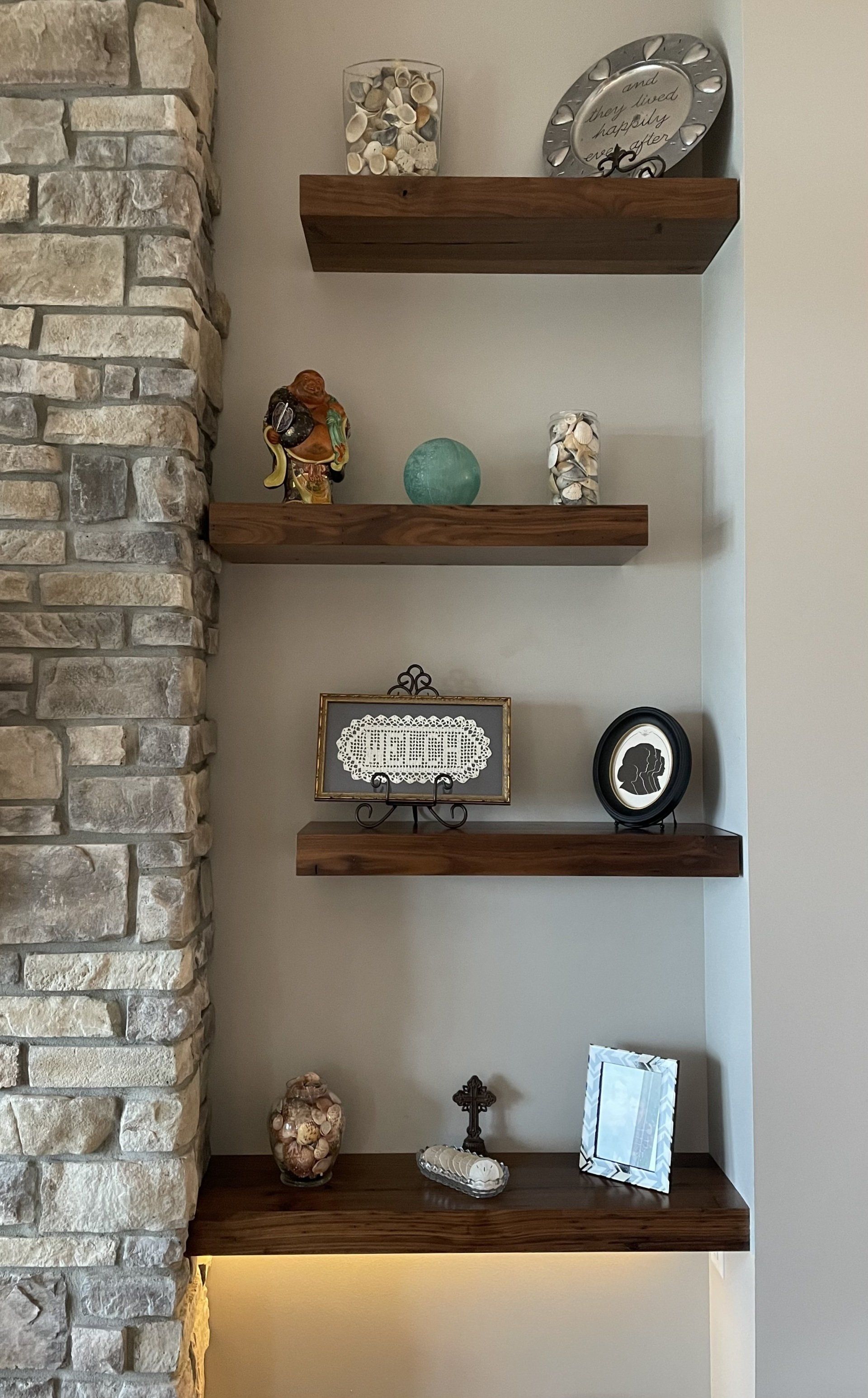 A wooden shelf with a clock on it is next to a stone wall.
