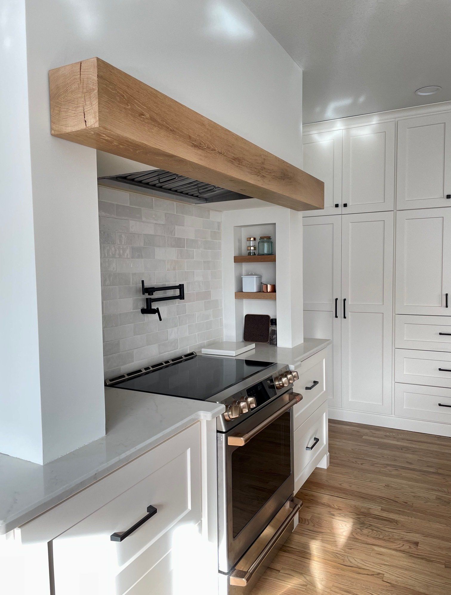 A kitchen with white cabinets , a stove , and a wooden beam above the stove.