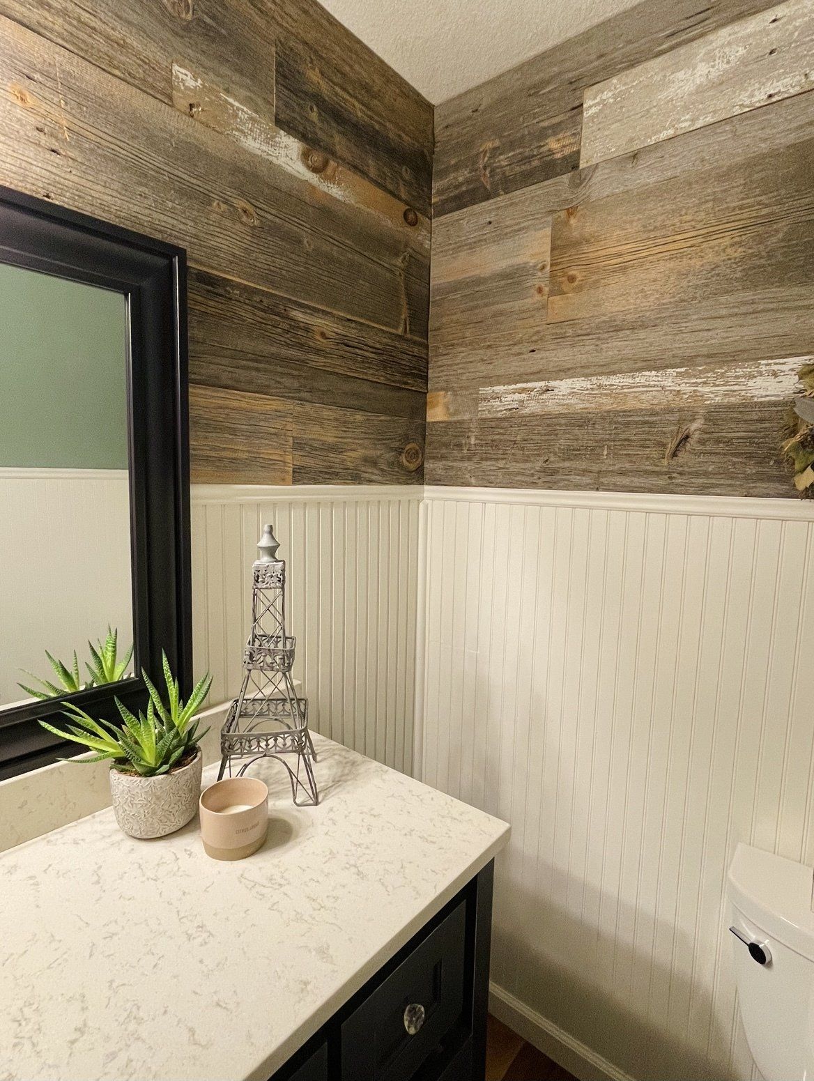 A bathroom with a sink , toilet , mirror and wood paneling on the walls.