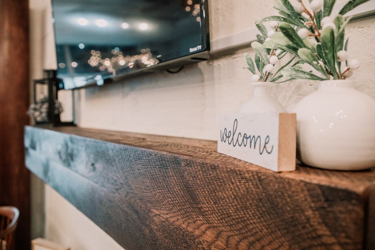 A welcome sign is sitting on a wooden shelf next to a vase of flowers.