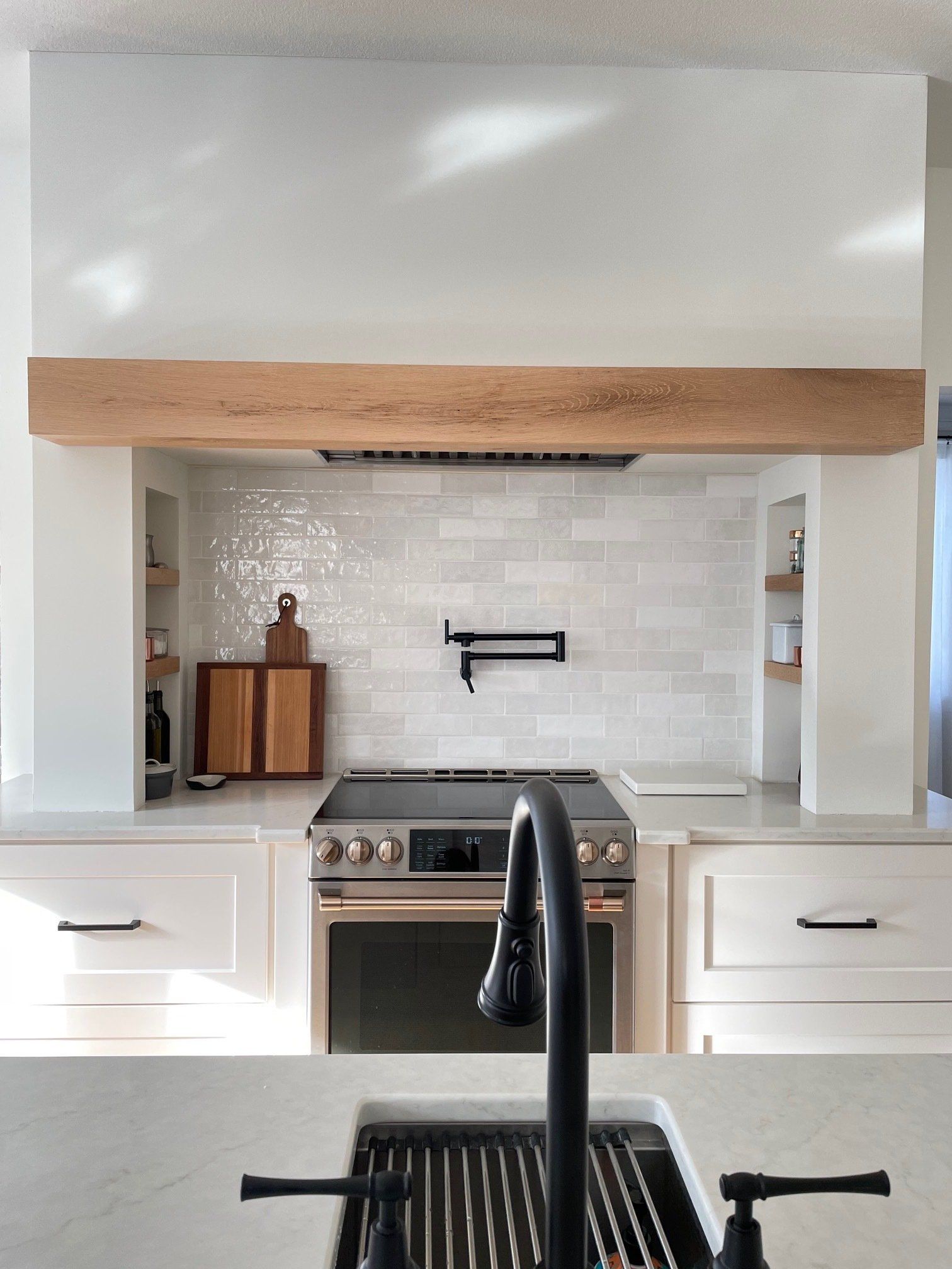 A kitchen with white cabinets , a stove , a sink , and a wooden beam above the stove.