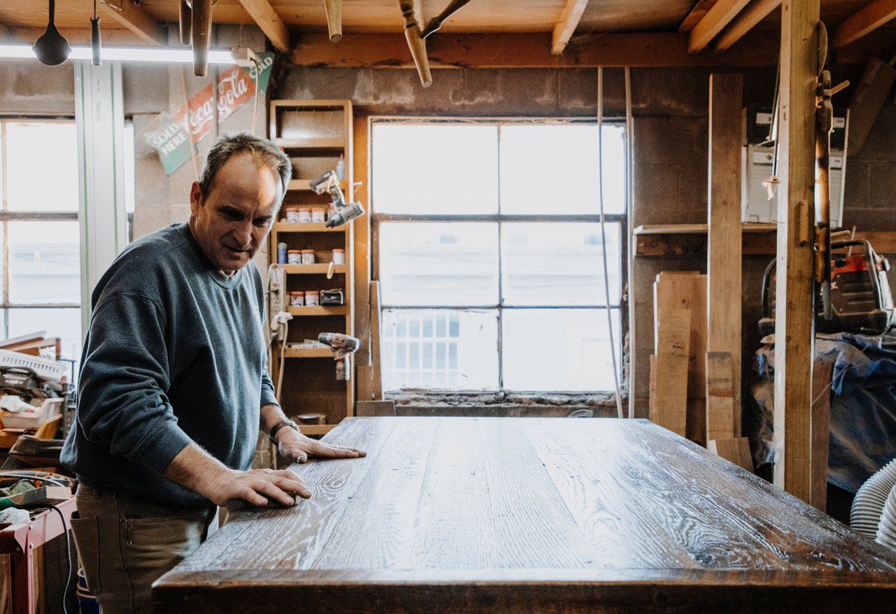 A man is working on a wooden table in a workshop.