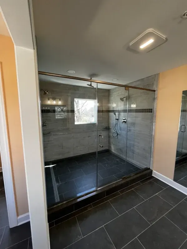 Glass shower with gray tile walls, dark floor, and chrome fixtures.