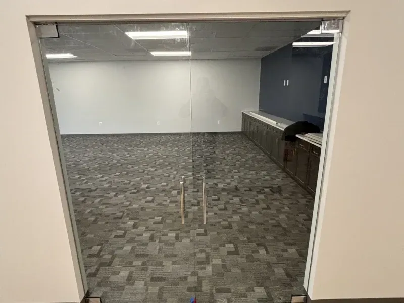 Glass double doors leading into an empty room with dark patterned carpet and built-in cabinetry.