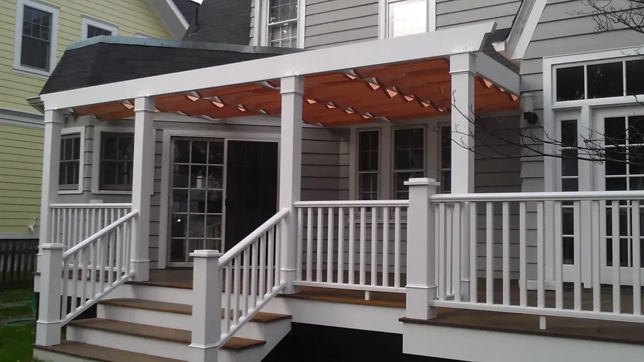 Wooden porch with white railing, steps, and orange awning, attached to a gray house.