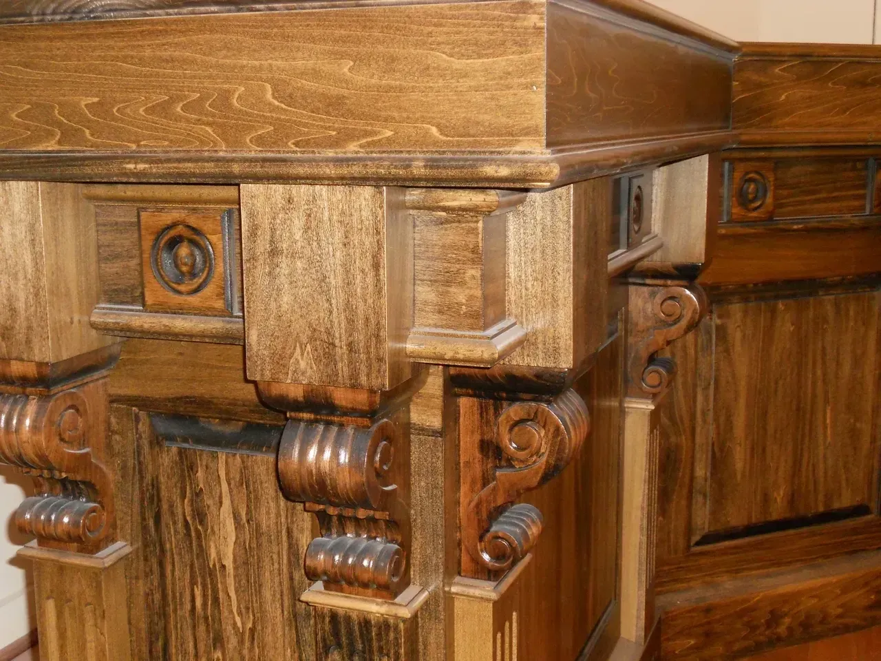 Ornate, dark-stained wooden furniture corner, featuring decorative brackets, panels, and carved details.