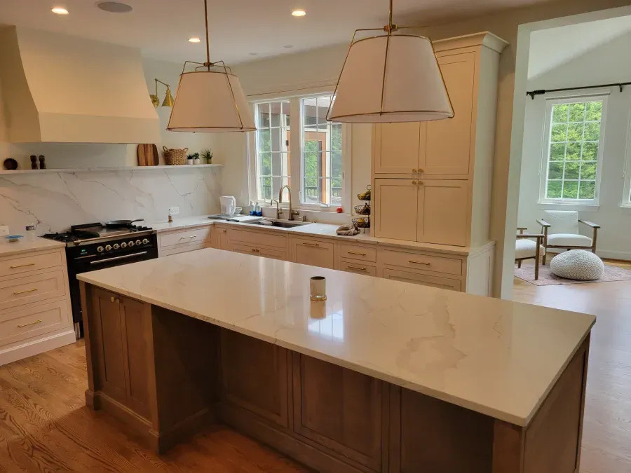 A bright kitchen with a large island, stove, white countertops, and wood cabinets. Two pendant lights hang over the island.