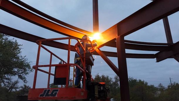 Sunlit steel beams of a construction frame with a red lift at dusk