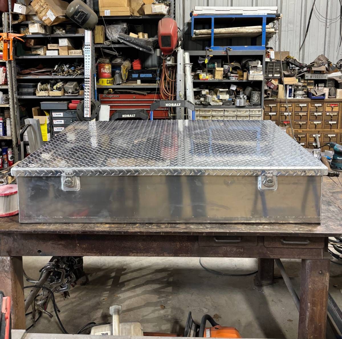Aluminum diamond-plate toolbox on a workbench in a cluttered workshop