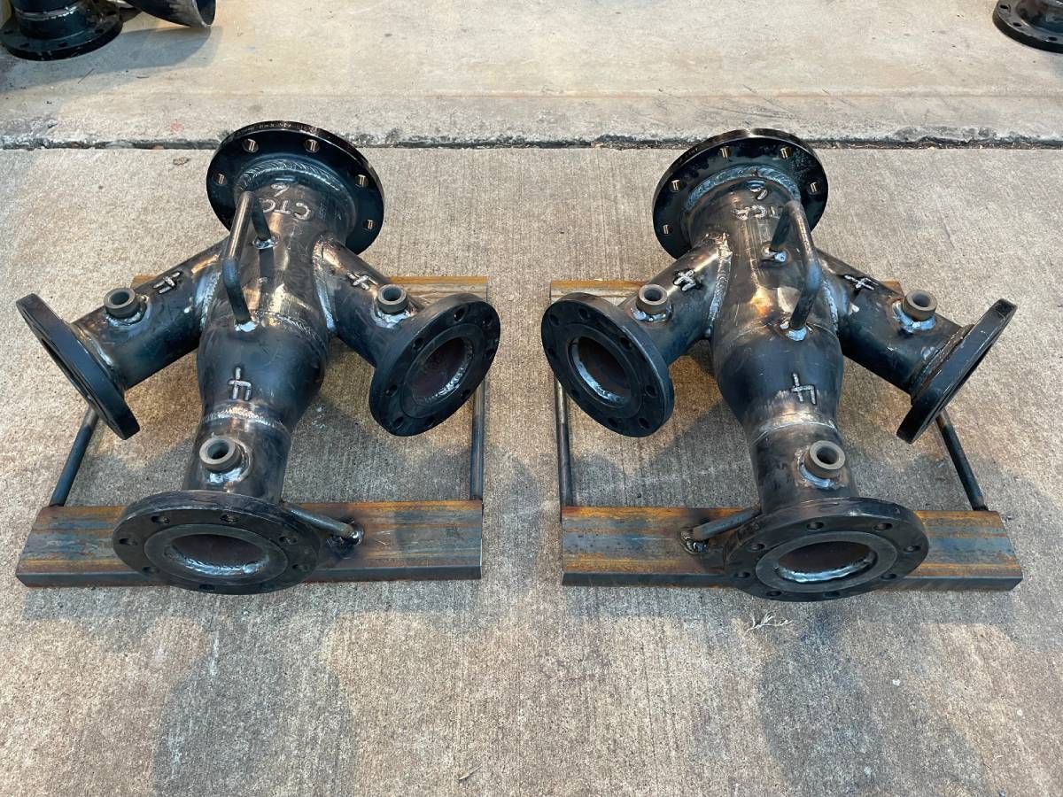 Two black cast-iron pipe fittings on wooden boards on a concrete floor