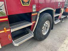 Red fire truck with silver steps and a large front wheel on pavement