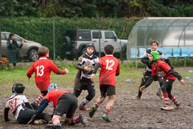 Un gruppo di ragazzi gioca a rugby su un campo fangoso.