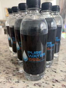 Rows of clear plastic water bottles with black caps on a granite countertop.