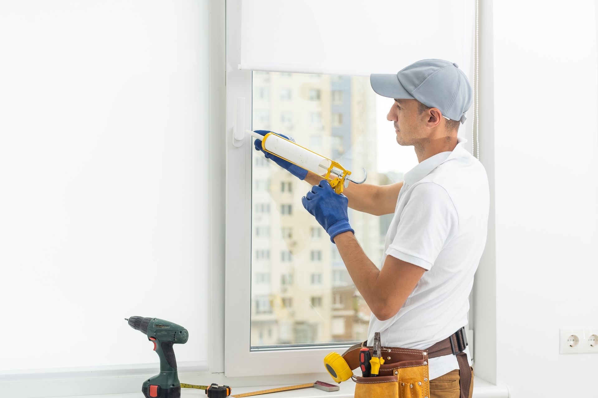 Contractor sealing a white vinyl window frame with caulk during a new window installation project.