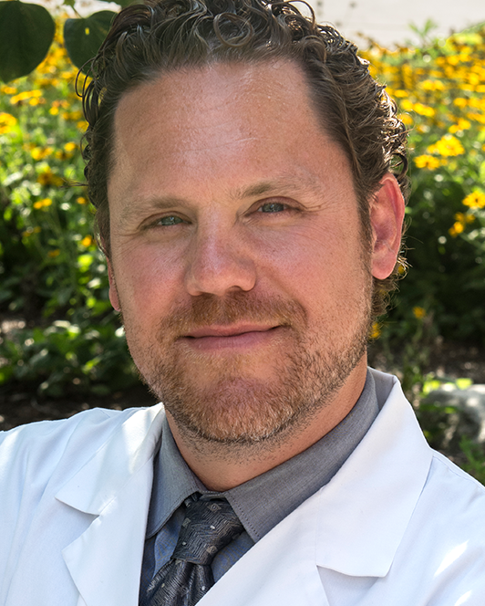 A man in a white coat and tie is smiling for the camera.