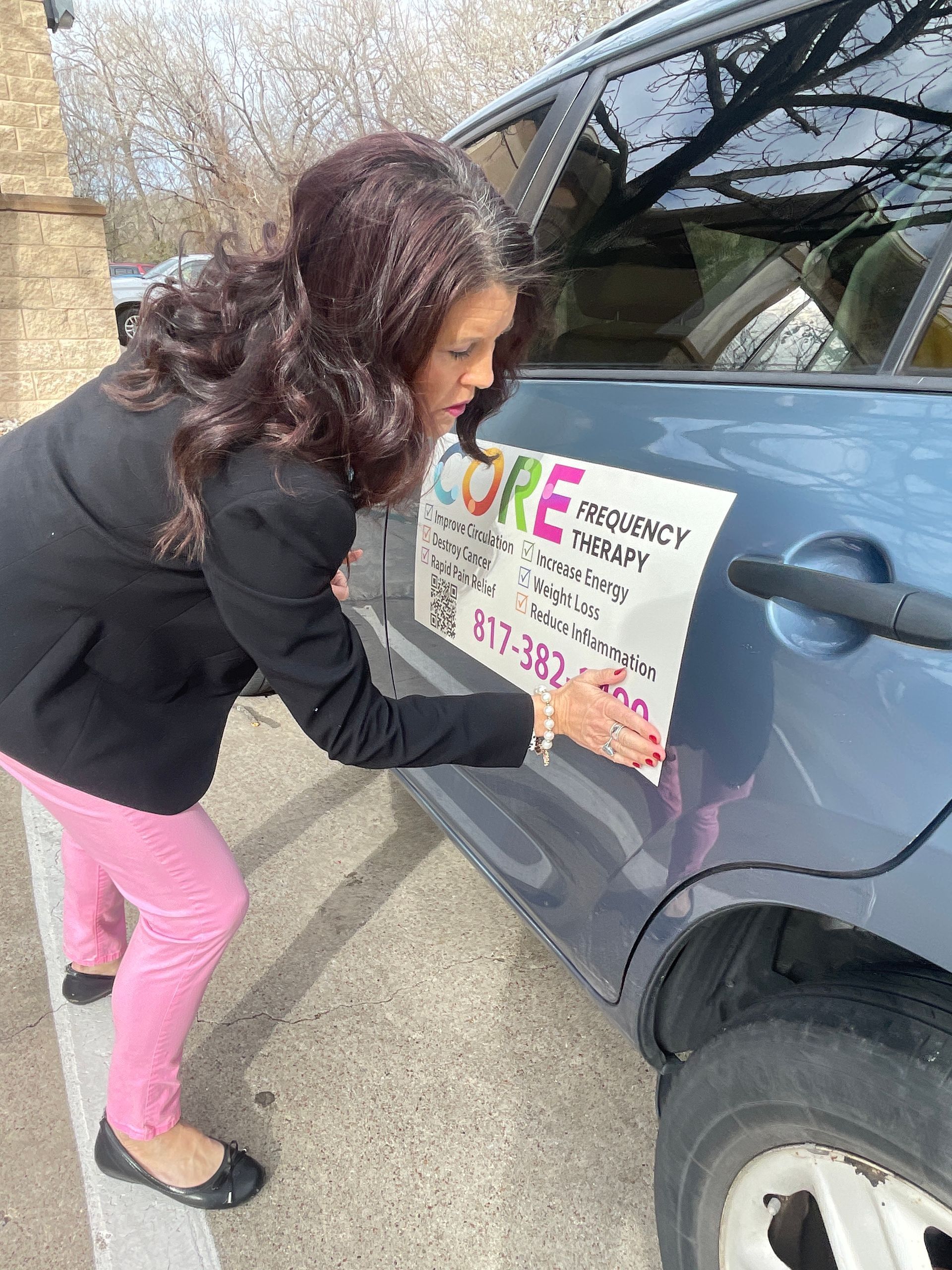 Woman placing a sign on the side of a gray SUV in a parking lot
