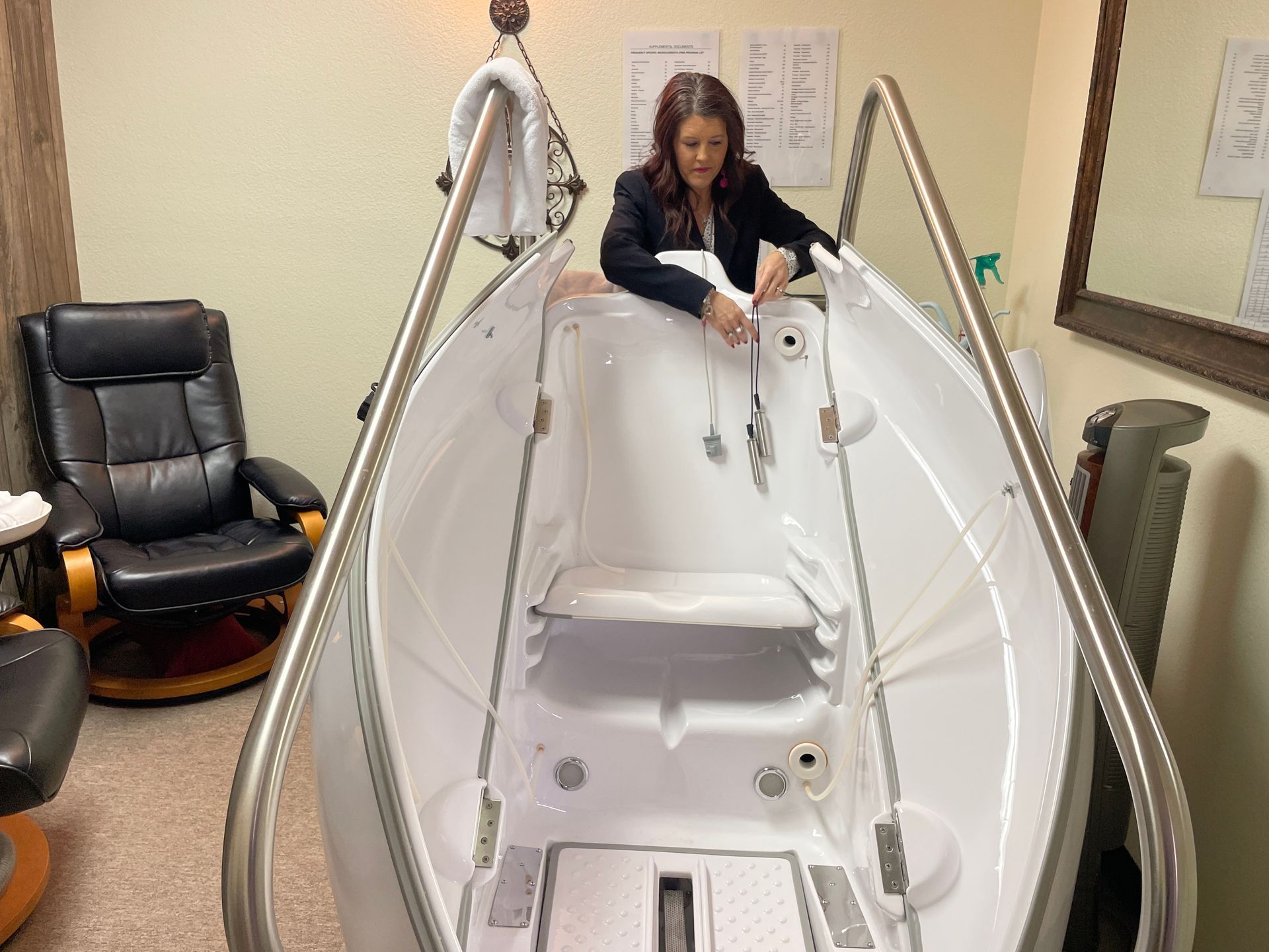 Woman in a white hyperbaric chamber, leaning over the open hatch in a clinical room.