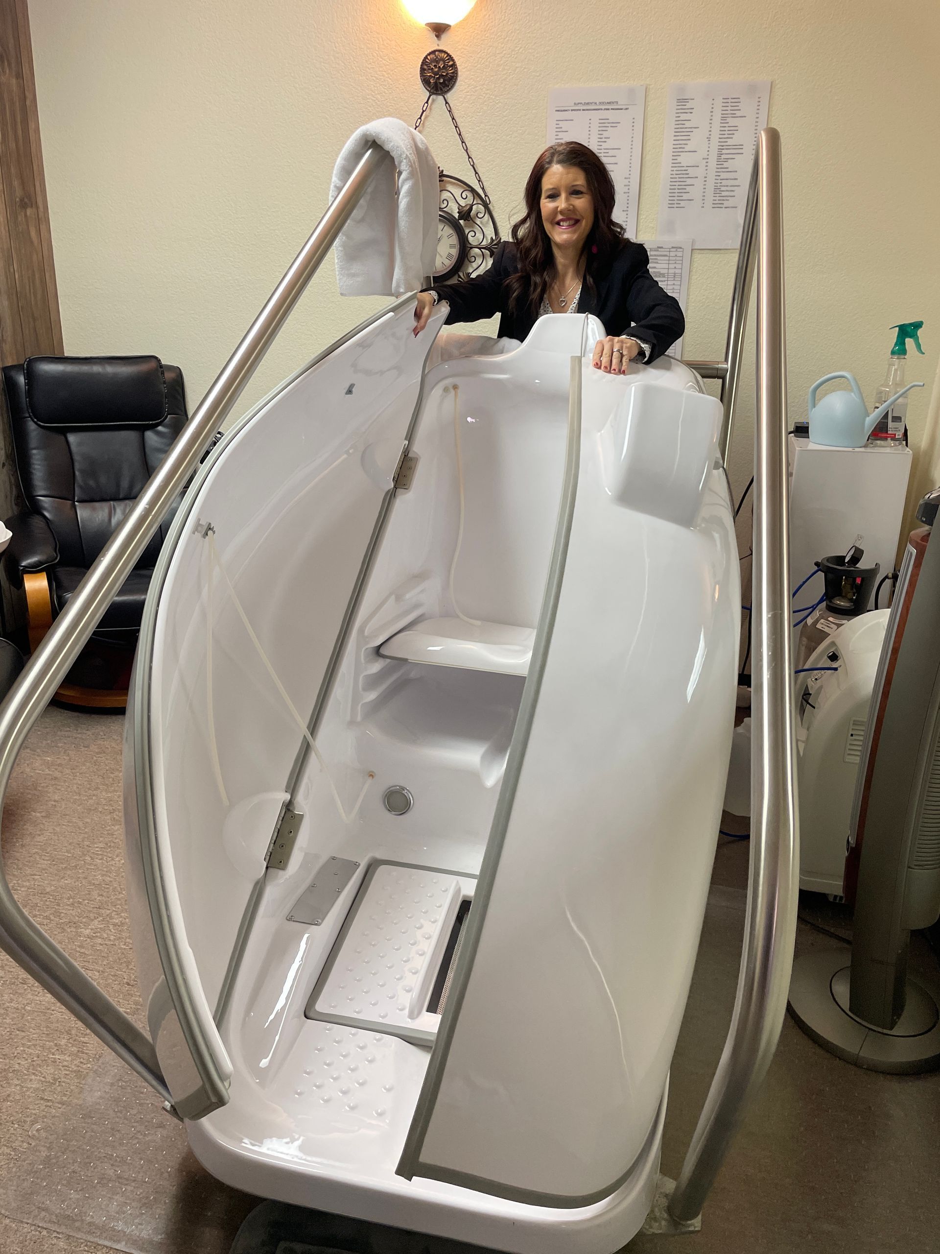 Woman standing inside a white pod-like wellness chamber in a treatment room
