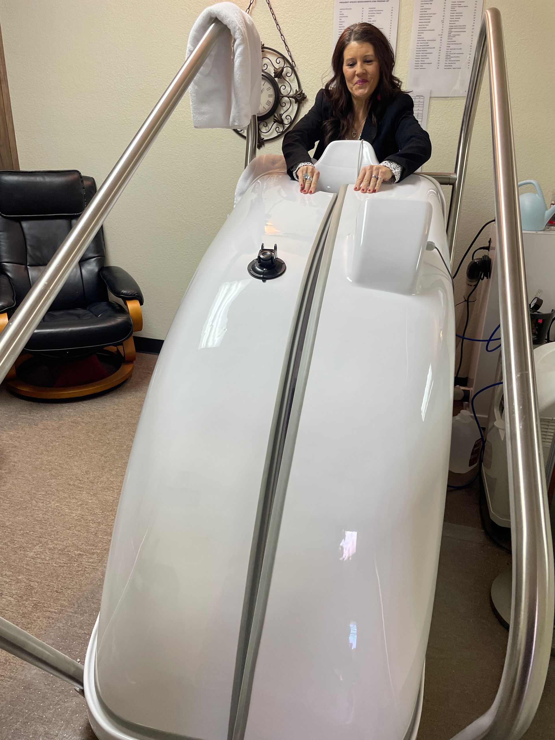 Person sitting inside a white hyperbaric chamber, smiling and holding a phone through the top opening