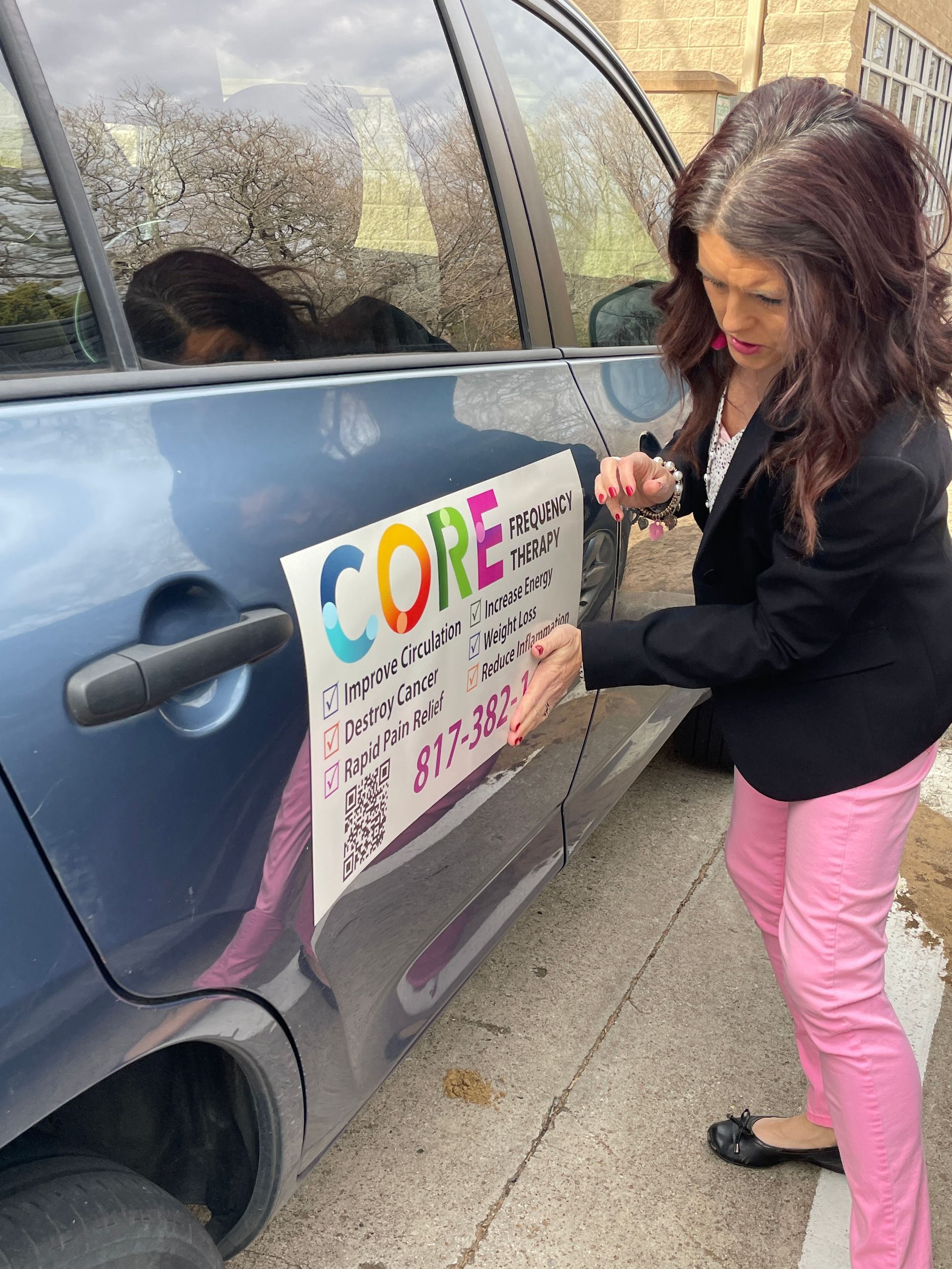 Woman placing a colorful sign on a parked blue car outside