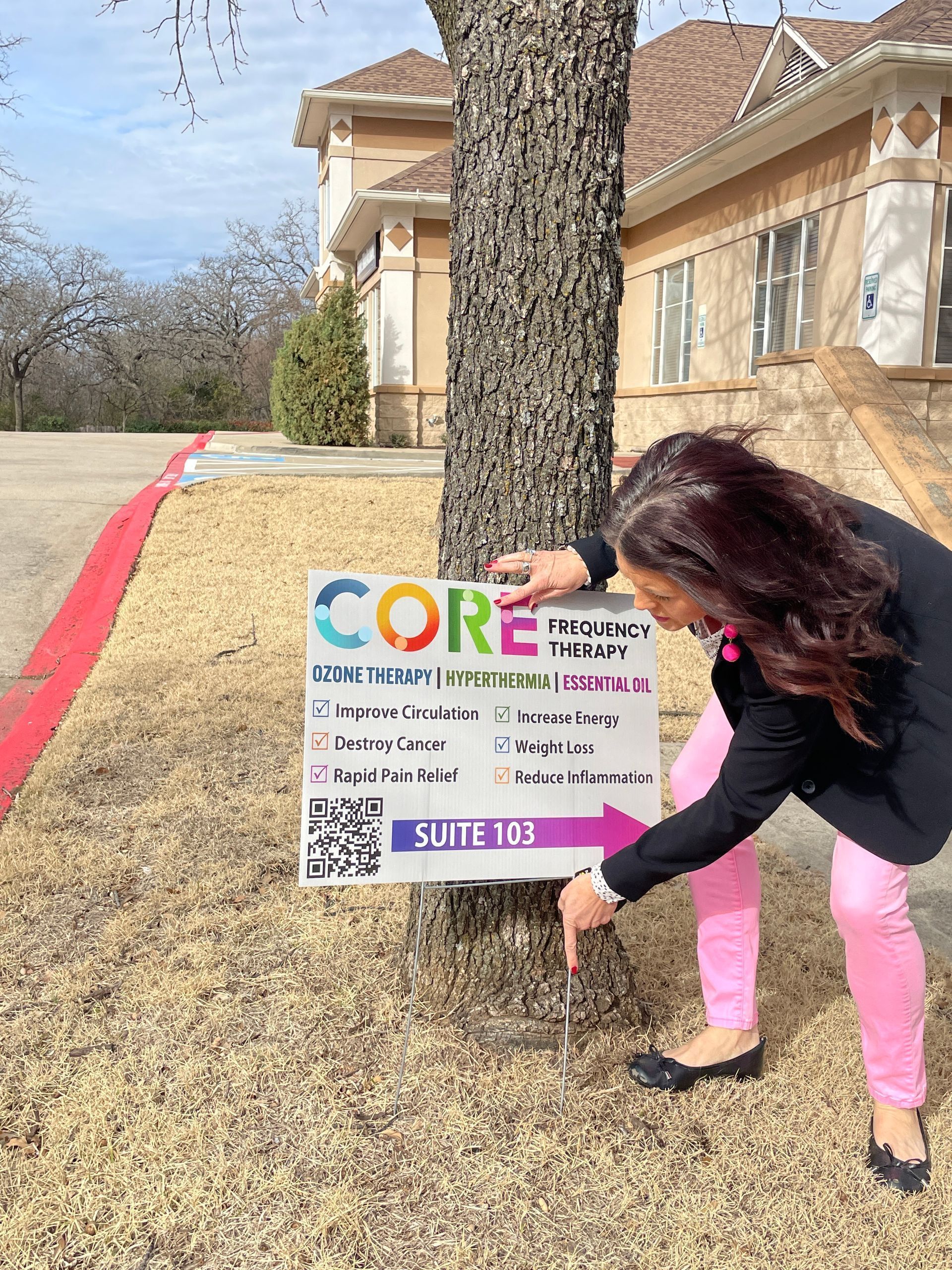 Woman placing a sign beside a tree on a suburban lawn near a house