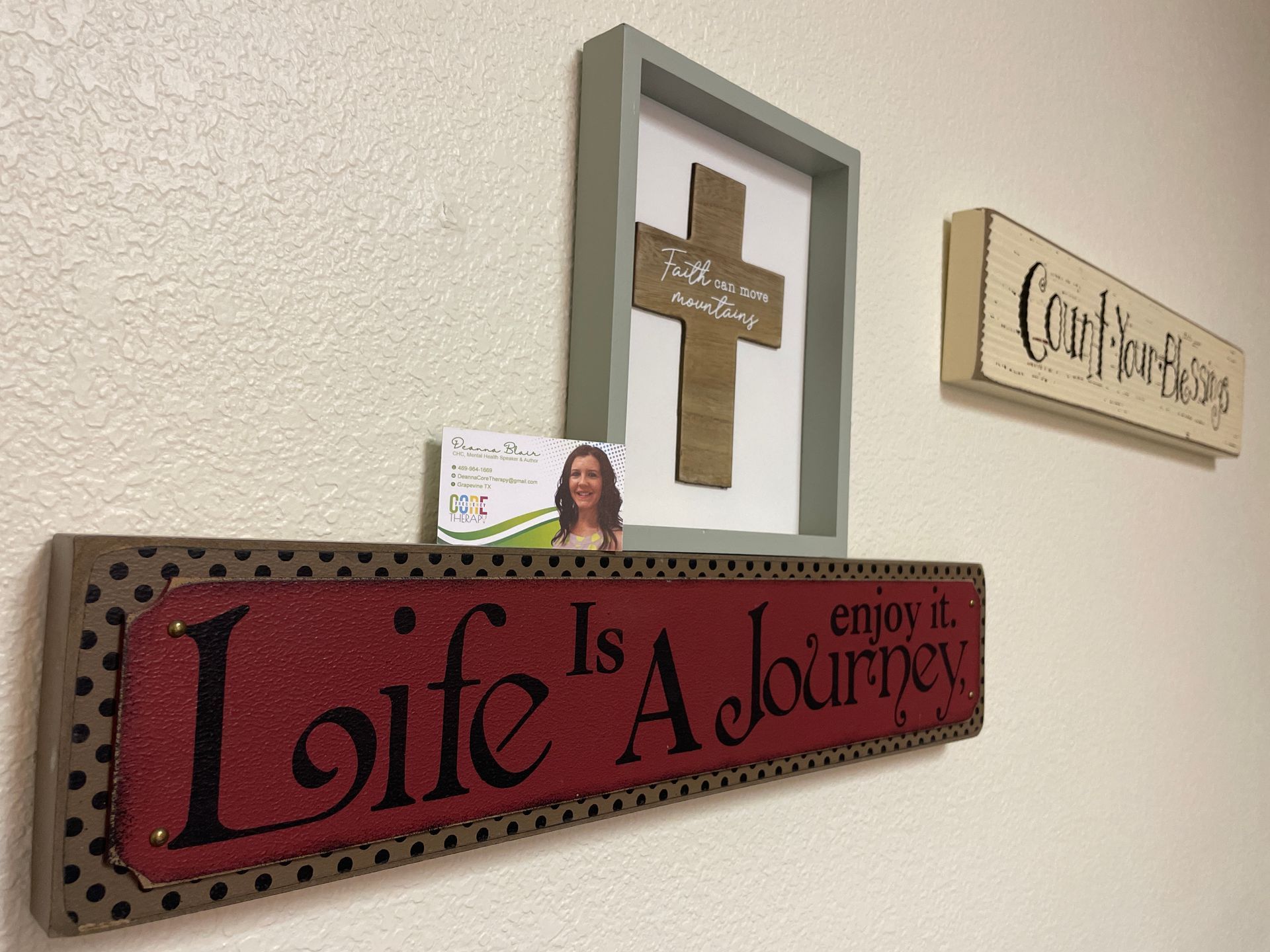 Wall decor with a cross, “Count your blessings” sign, and red “Life is a Journey” plaque