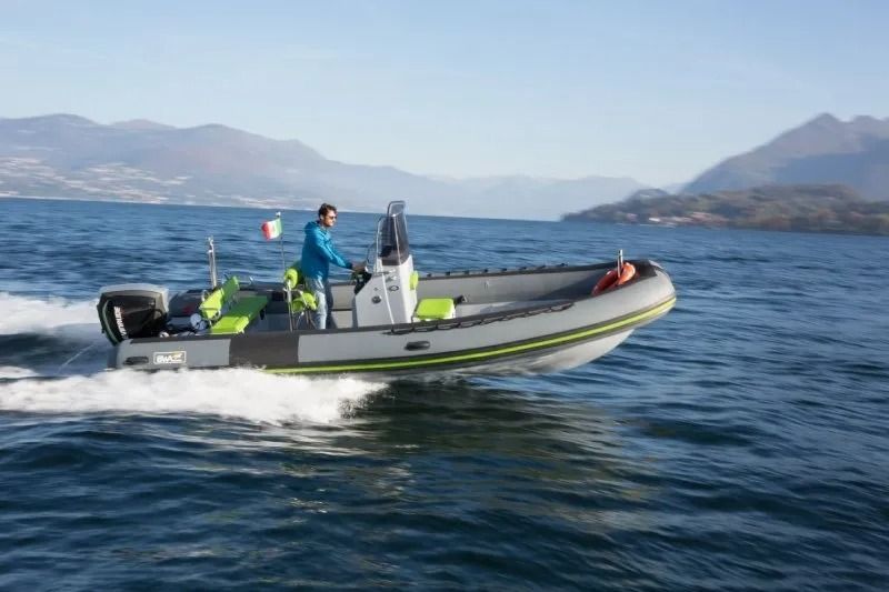 Un gommone con scafo rigido sfreccia sull'acqua, con le montagne sullo sfondo e una persona al timone.