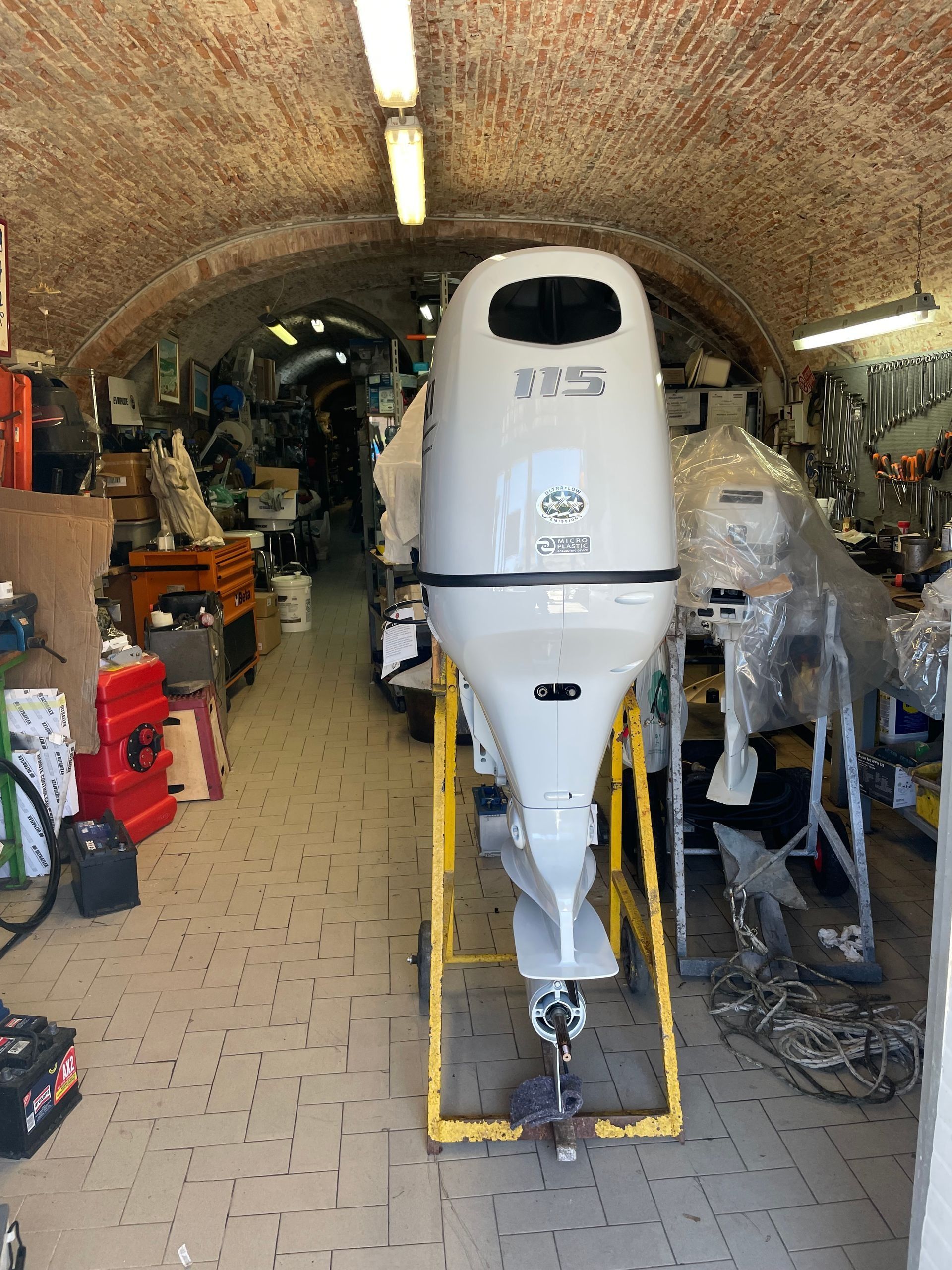 Motore fuoribordo bianco su un supporto giallo all'interno di un'officina disordinata.