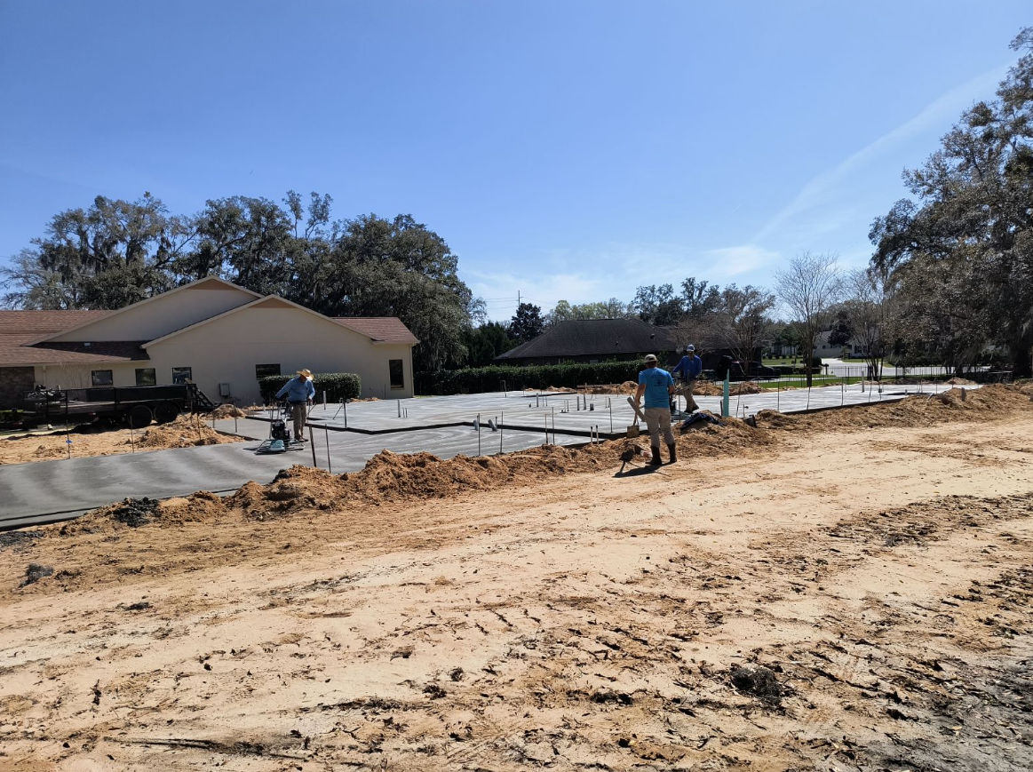 A group of people are standing in a dirt field in front of a house. Project done by C1 Foundations