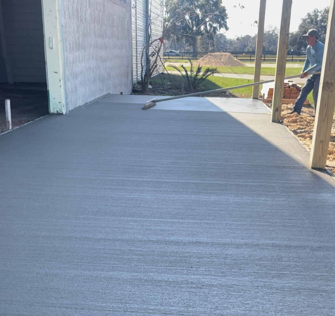 A man is standing on a concrete porch with a broom. Project done by C1 Foundations